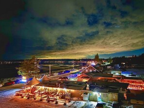 Espaço ao ar livre bem iluminado com um prédio de madeira, tendas e uma estrada pavimentada.