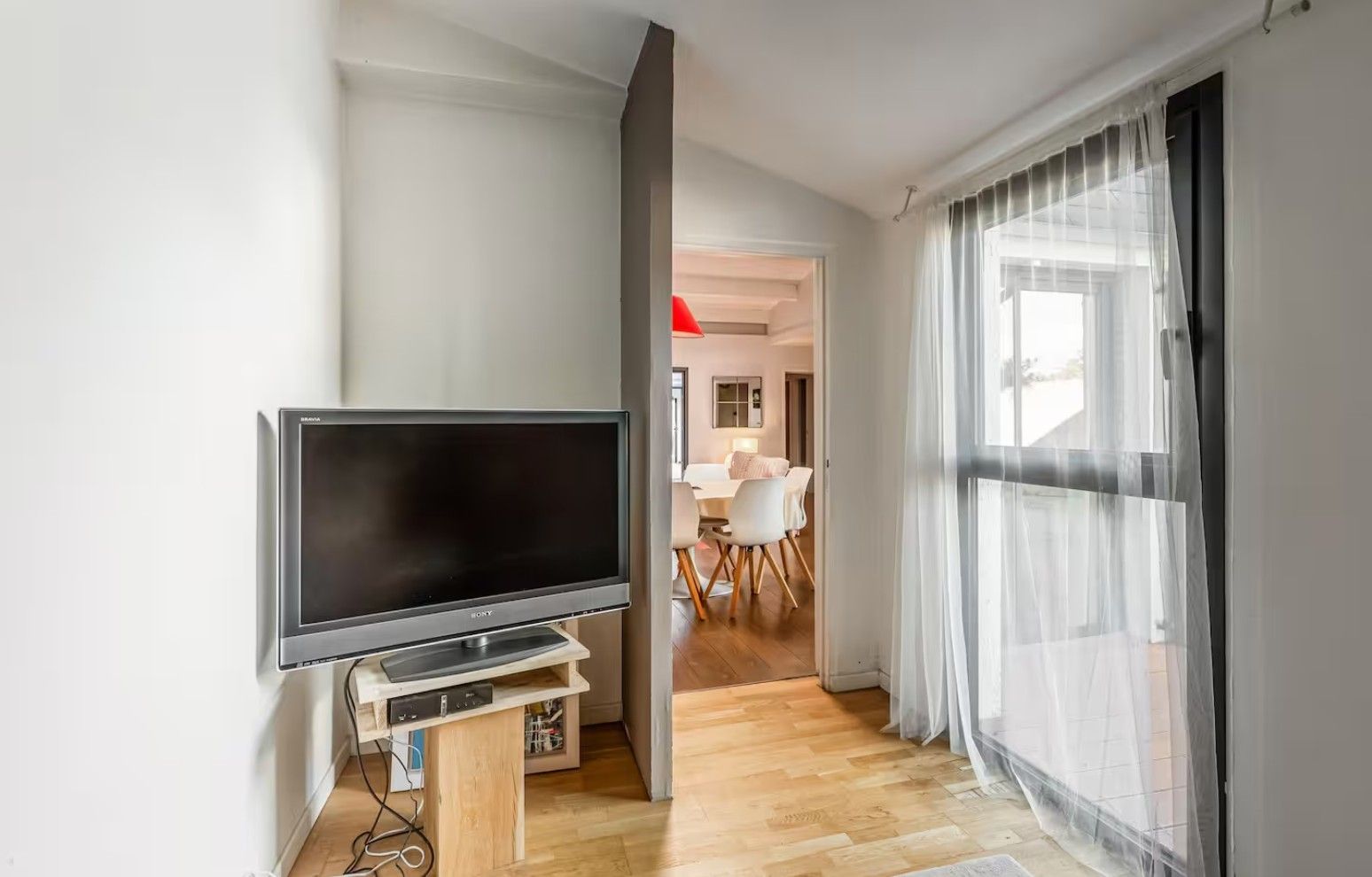 Una sala de estar moderna con televisor de pantalla plana, piso de madera y un comedor con mesa y sillas blancas.