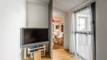 Una sala de estar moderna con televisor de pantalla plana, piso de madera y un comedor con mesa y sillas blancas.