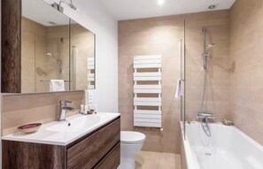 Une salle de bain moderne équipée d’une baignoire, d’une douche, de toilettes et d’un meuble-lavabo avec un miroir.