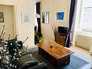 A living room with a sofa, coffee table, and a television. There are framed pictures on the wall and a window with curtains. - Authentic and Welcoming - Heart of Historic La Rochelle (La Rochelle)