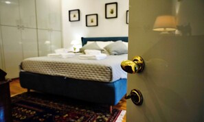 Un dormitori amb llit, una taula de nit, una làmpada i una porta amb pom d'or.