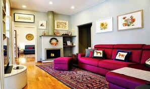 A living room with a fireplace, a red sofa, a patterned rug, and various wall decorations. - CENTRAL ROME APARTMENT WITH TERRACE, ENSUITE BEDROOM AND MODERN COMFORTS (Roma)