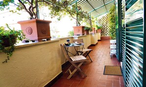A covered outdoor seating area with terracotta planters, a wooden chair, and a table with a coffee pot. - CENTRAL ROME APARTMENT WITH TERRACE, ENSUITE BEDROOM AND MODERN COMFORTS (Roma)
