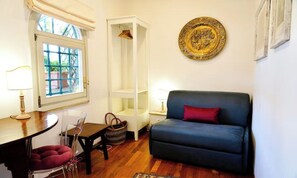 A room with a blue sofa, a white shelving unit, a dining table with chairs, and a window with blue bars. - CENTRAL ROME APARTMENT WITH TERRACE, ENSUITE BEDROOM AND MODERN COMFORTS (Roma)