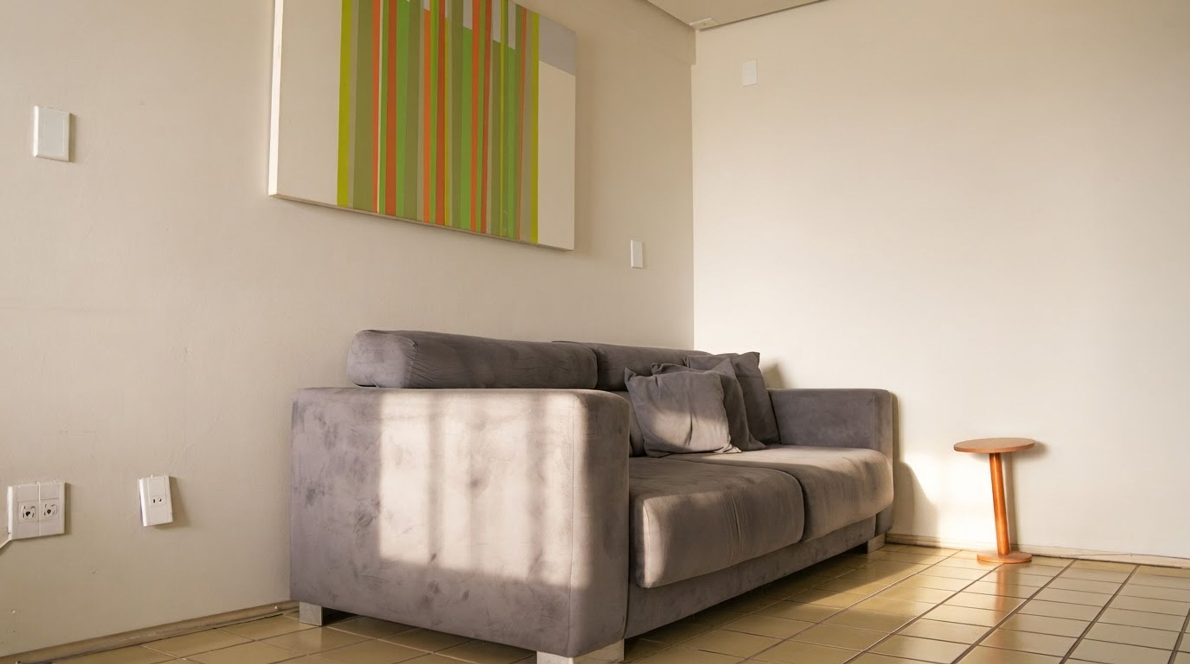 A modern living room with a grey sofa, a small round table, and a colorful abstract painting on the wall.
