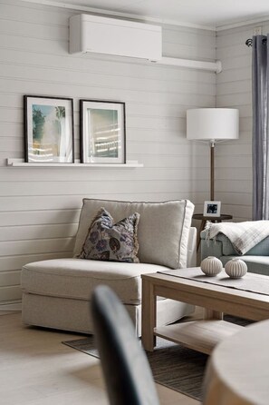 A modern living room with a sofa, a coffee table, and a floor lamp. There are two framed pictures on the wall and a small table with a clock. - Winter Garden Apartment | Tromsø City (Tromsø)