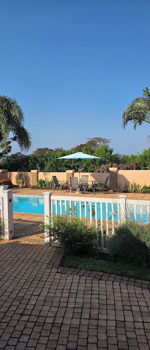 Un espace piscine avec une terrasse en briques, des chaises longues et une table avec un parasol.