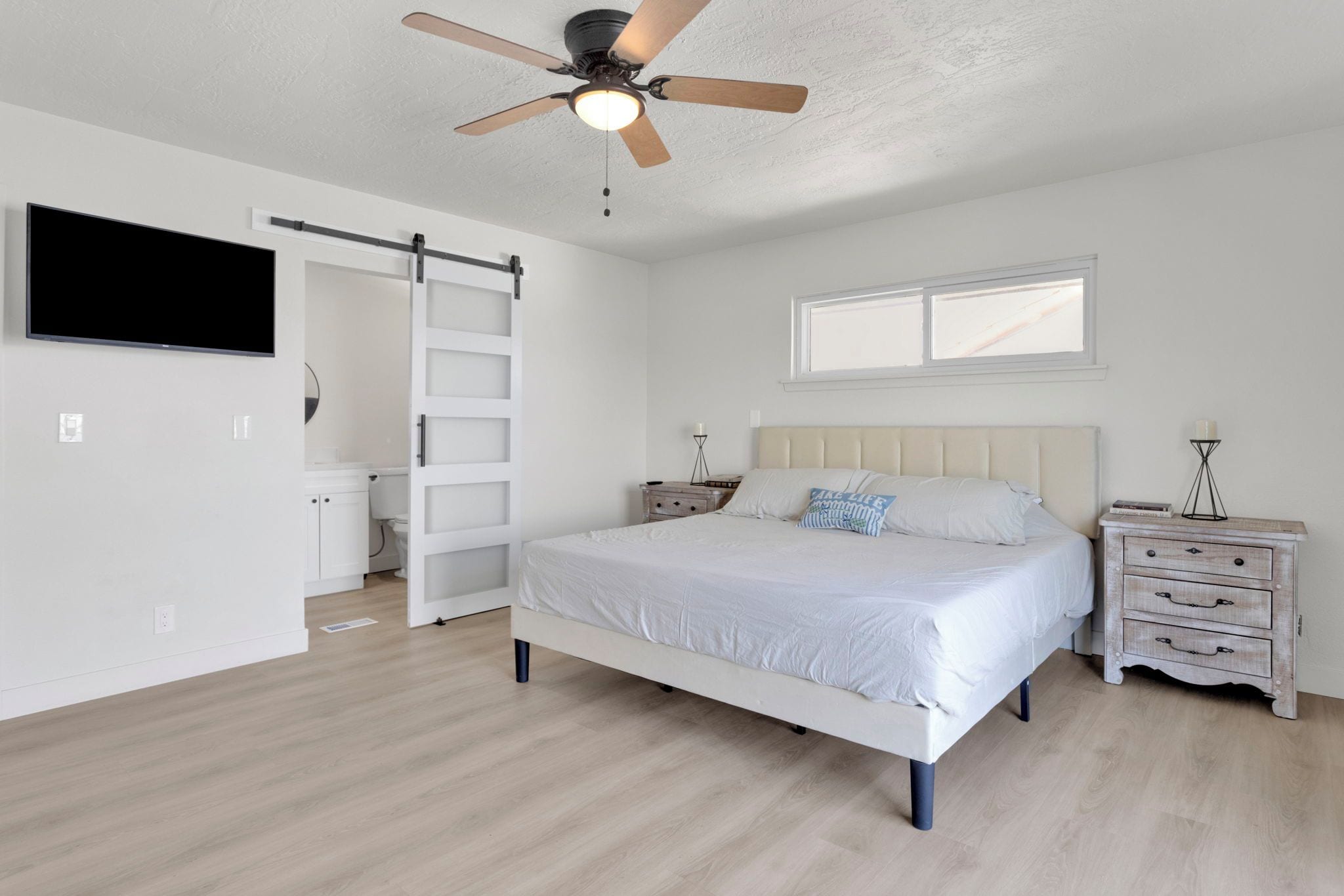 Un dormitorio con cama, mesita de noche, cómoda, ventilador de techo, ventana y puerta.