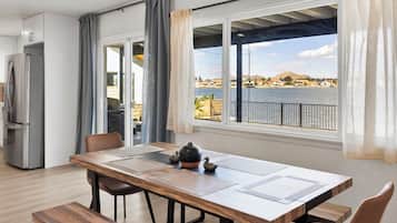 Un comedor moderno con una mesa de madera, sillas y vistas a un lago y edificios.