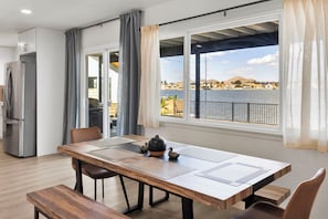 Een moderne eethoek met een houten tafel, stoelen en uitzicht op een meer en gebouwen.