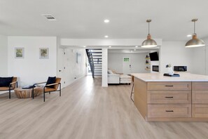 Een moderne keuken met een centraal eiland, hanglampen en een trap naar een vide.