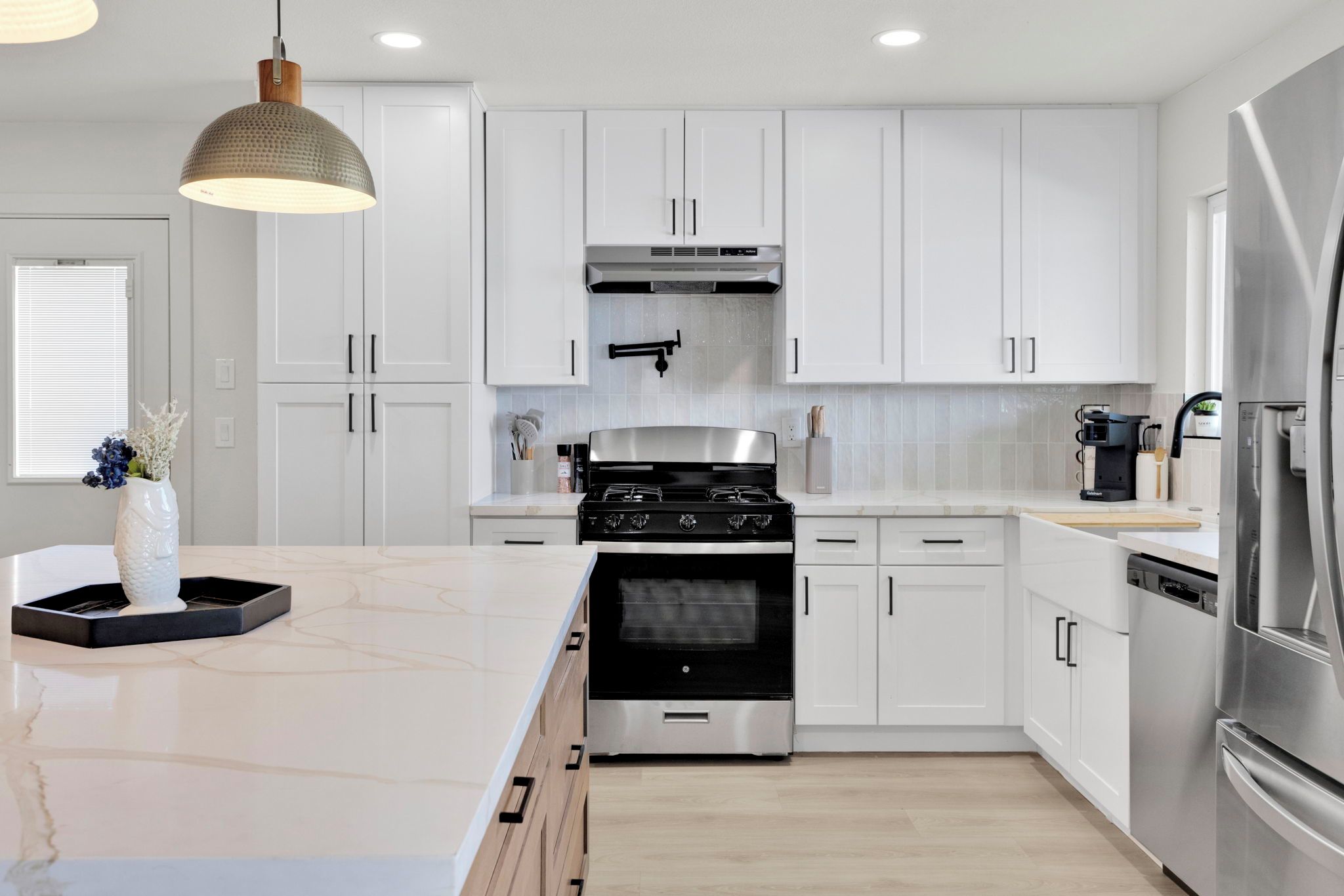 Una cocina moderna con armarios blancos, estufa de acero inoxidable y una isla grande con encimera de mármol.