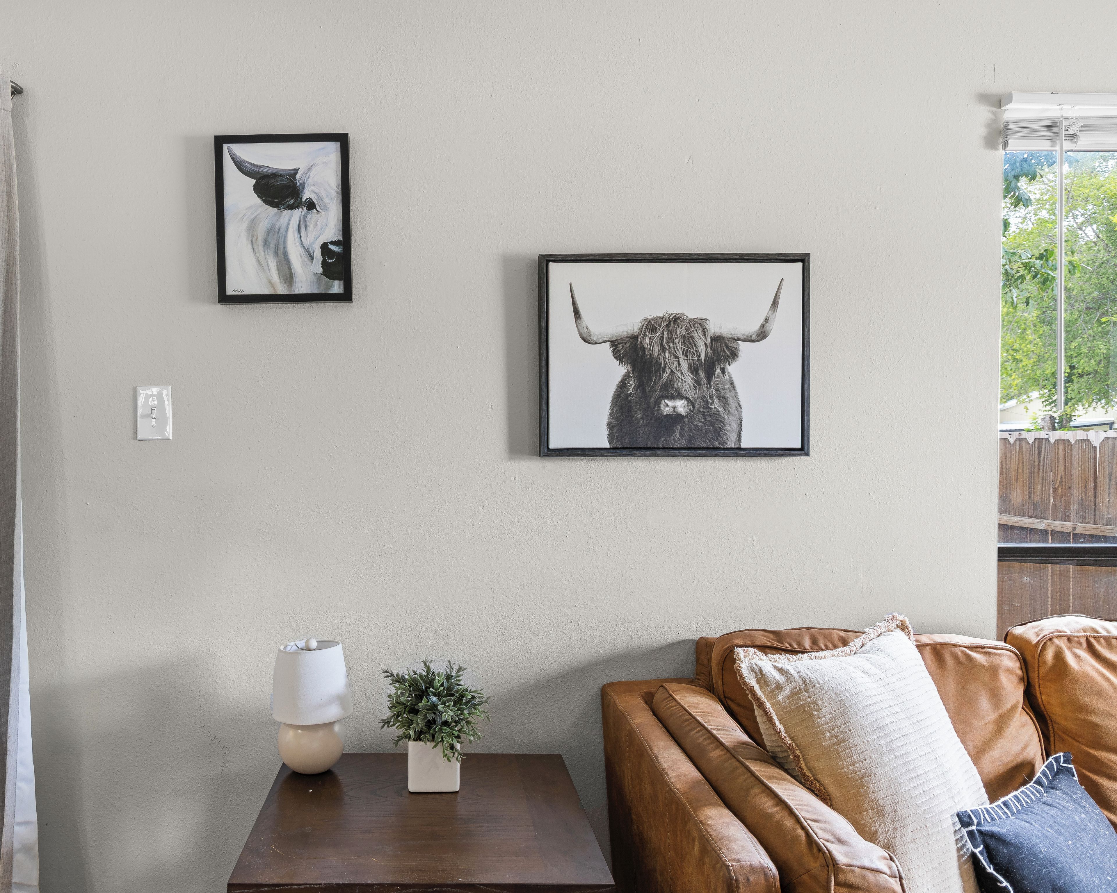 A living room with a brown leather couch, a small table with a lamp and a plant, and two framed pictures on the wall.