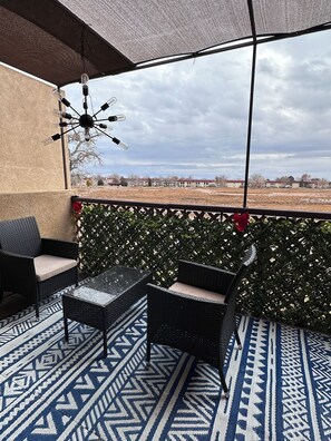 A covered outdoor seating area with a patterned floor, a wall-mounted light fixture, and a view of distant buildings. - Modern 2-bedroom condo close to Hospitals and Shops-centrally located Rio Rancho (Rio Rancho)