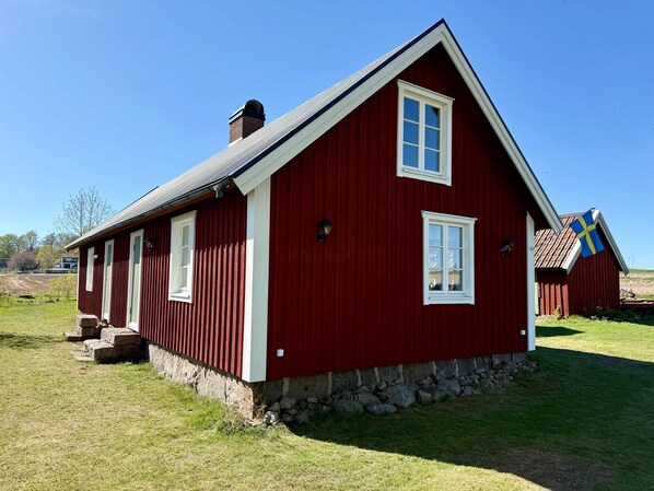 Una casa de madera roja con zócalo de piedra, una chimenea y una bandera.