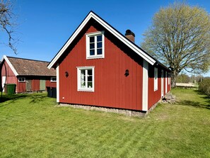 Una casa de madera roja con techo a dos aguas, chimenea y una ventana pequeña.