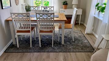 Un coin repas avec une table en bois et des chaises blanches, un tapis noir et une plante en pot.
