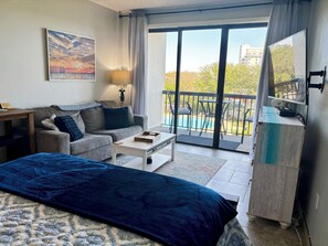 Ein Hotelzimmer mit Sofa, Couchtisch, Bett, Fernseher und Balkon mit Pool.