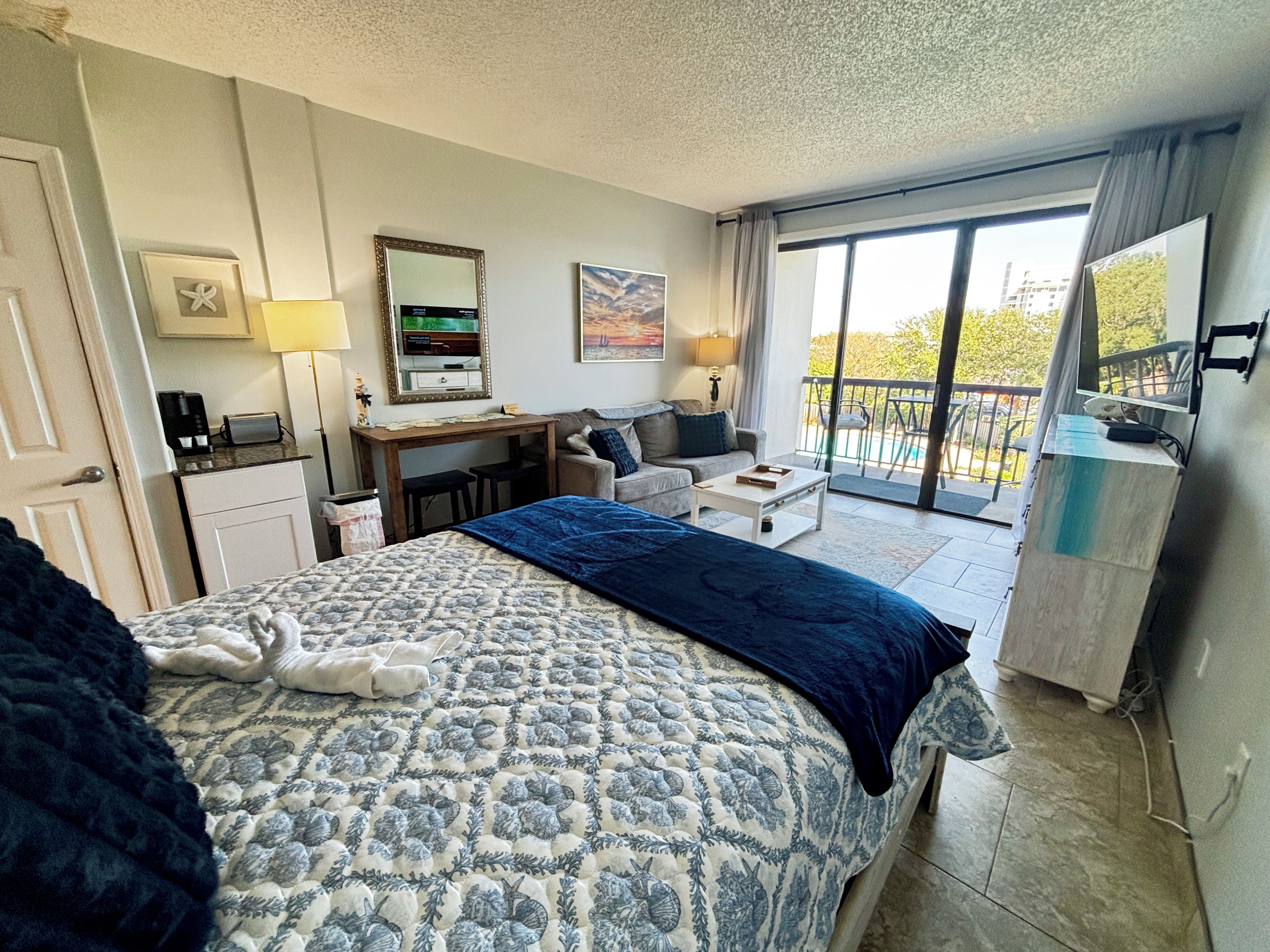A hotel room with a bed, a desk, a sofa, and a balcony with a view.