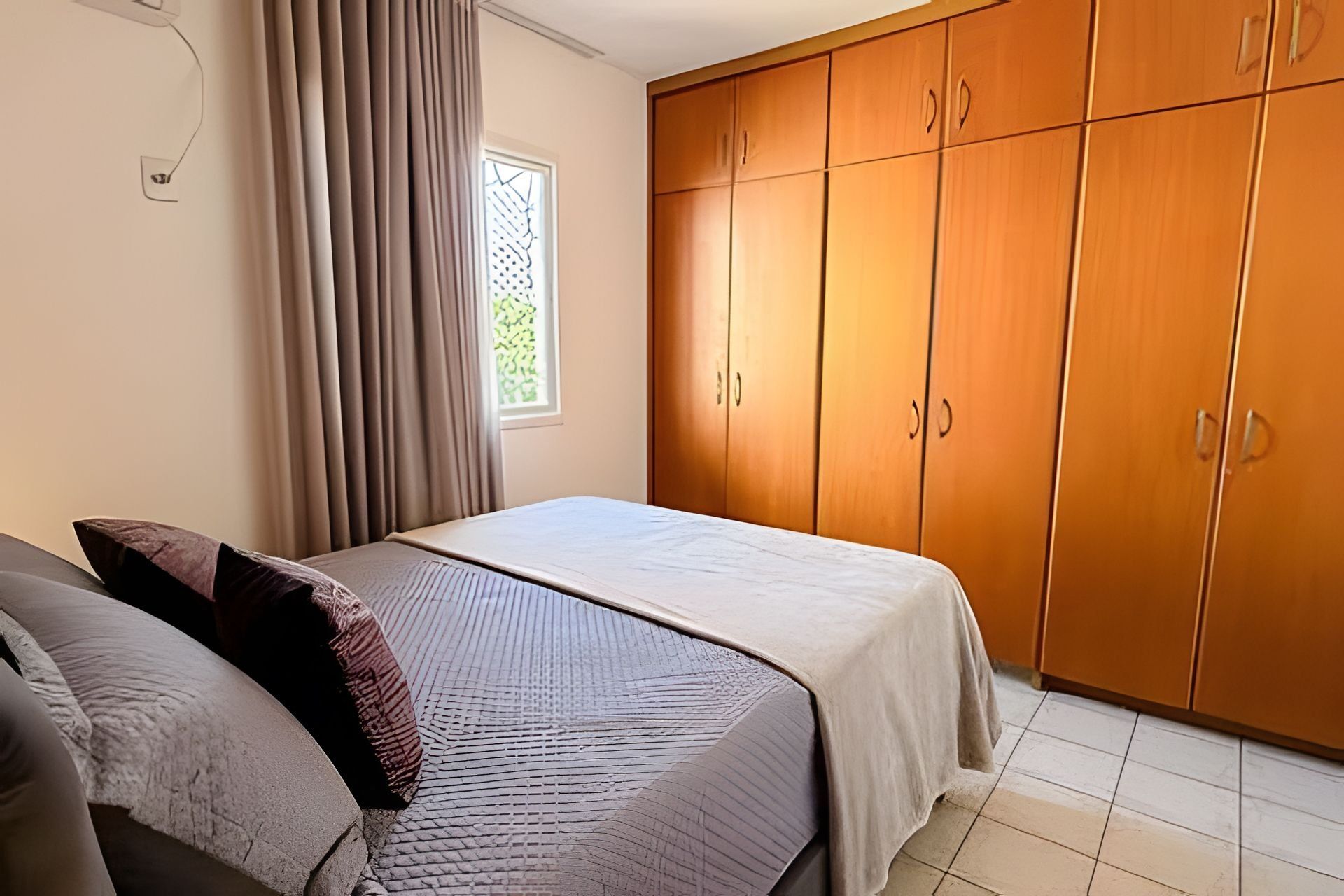 Una camera da letto con un letto, un armadio, una finestra con tende e un pavimento piastrellato.
