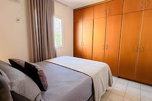 Un dormitorio con cama, armario, ventana con cortinas y suelo de baldosas.