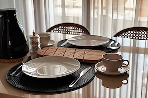 Una mesa de comedor dispuesta con platos, cubiertos, una taza y una cafetera.