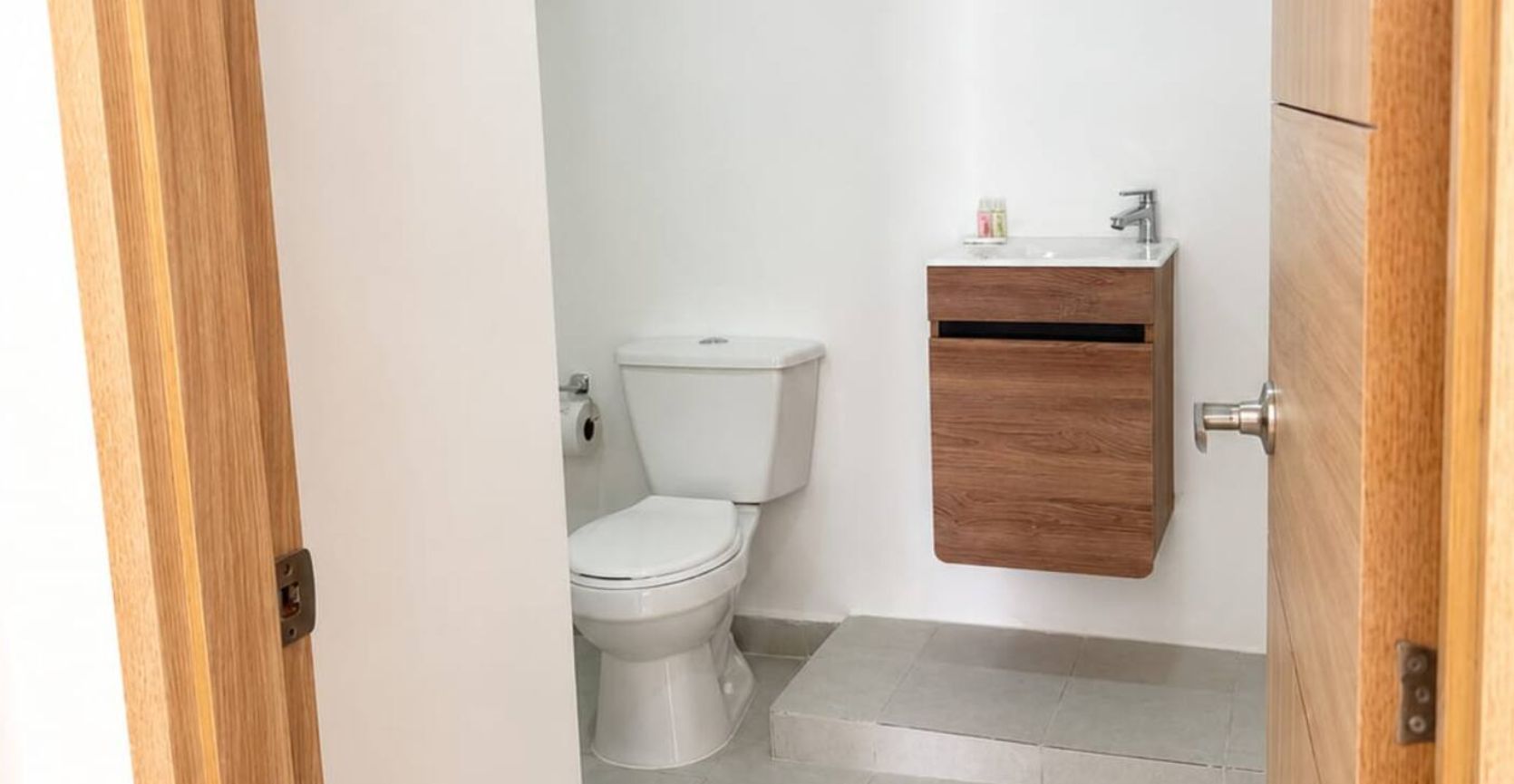 Un bany amb vàter, un armari de fusta i una porta.
