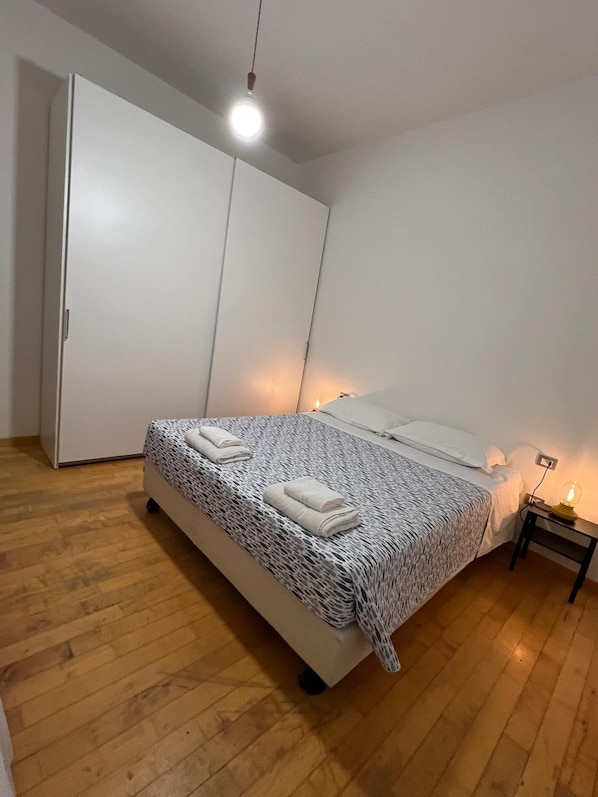 Una camera da letto con un letto, un armadio, un comodino con una lampada e un pavimento in legno.