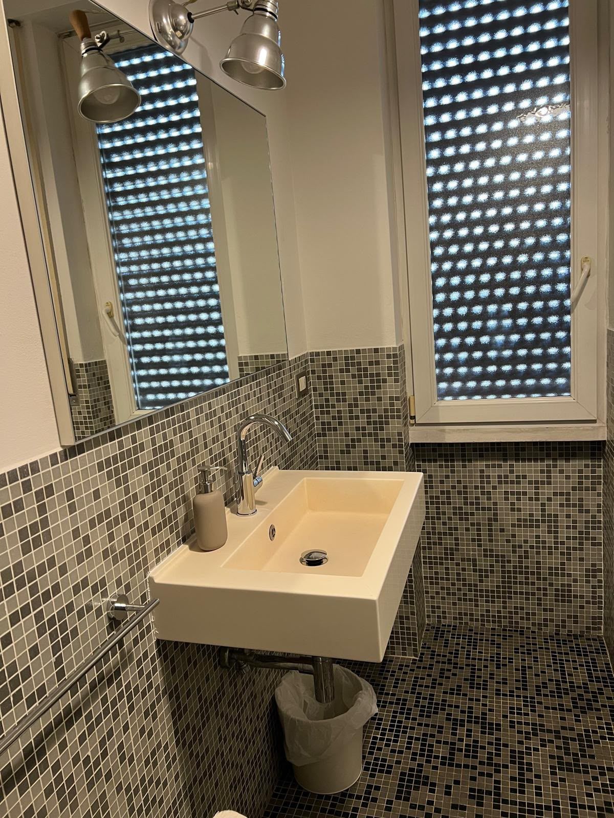 A bathroom with a white sink, a mirror, and a window with a patterned blind.