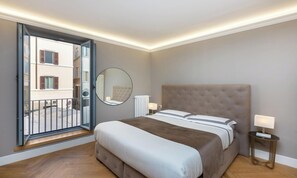 Ein Schlafzimmer mit einem Bett, einem runden Spiegel, Nachttischlampen und Blick durch eine geöffnete Tür.