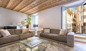 Ein modernes Wohnzimmer mit einer Sofagarnitur, einem Couchtisch und Blick auf eine Stadtkulisse durch große Fenster.