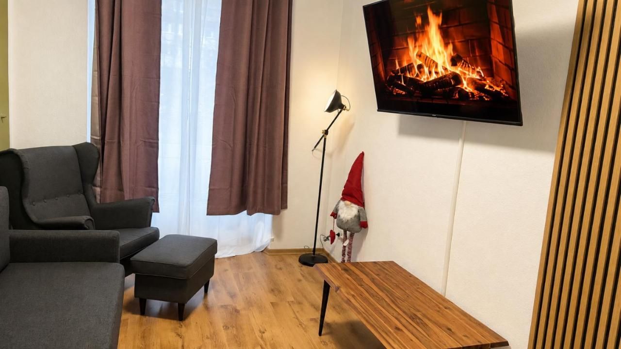 A living room with a sofa, ottoman, floor lamp, and a television displaying a fireplace.