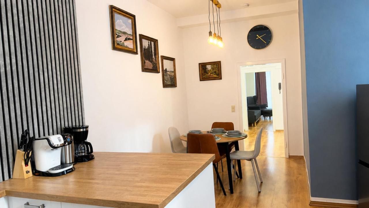 A modern kitchen with a wooden countertop, a coffee machine, and a dining area with a table and chairs.