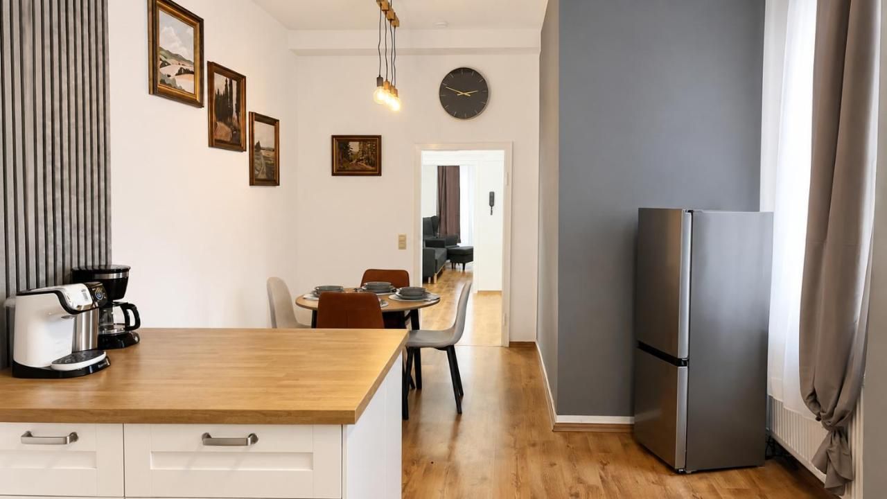 A modern kitchen with a wooden countertop, a refrigerator, and a dining area with chairs and a table.