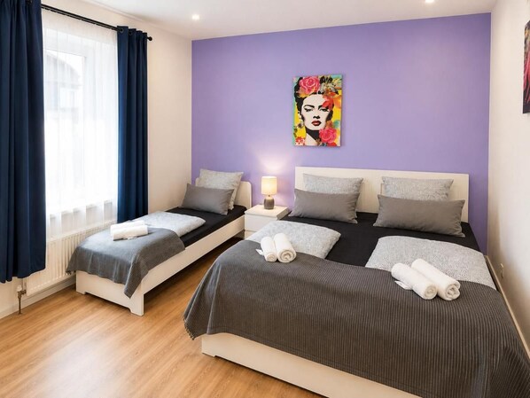 Een hotelkamer met twee bedden, een raam met gordijnen, een muur met een schilderij en een nachtkastje met een lamp.