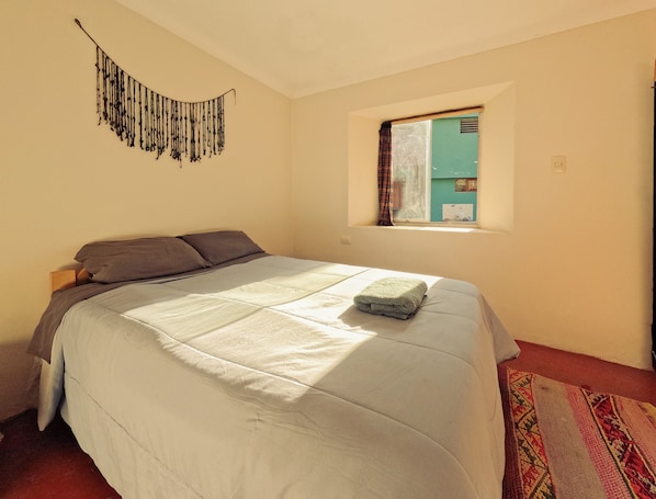 Un dormitorio con una cama, una ventana con cortinas, un tapiz en la pared y una alfombra estampada.