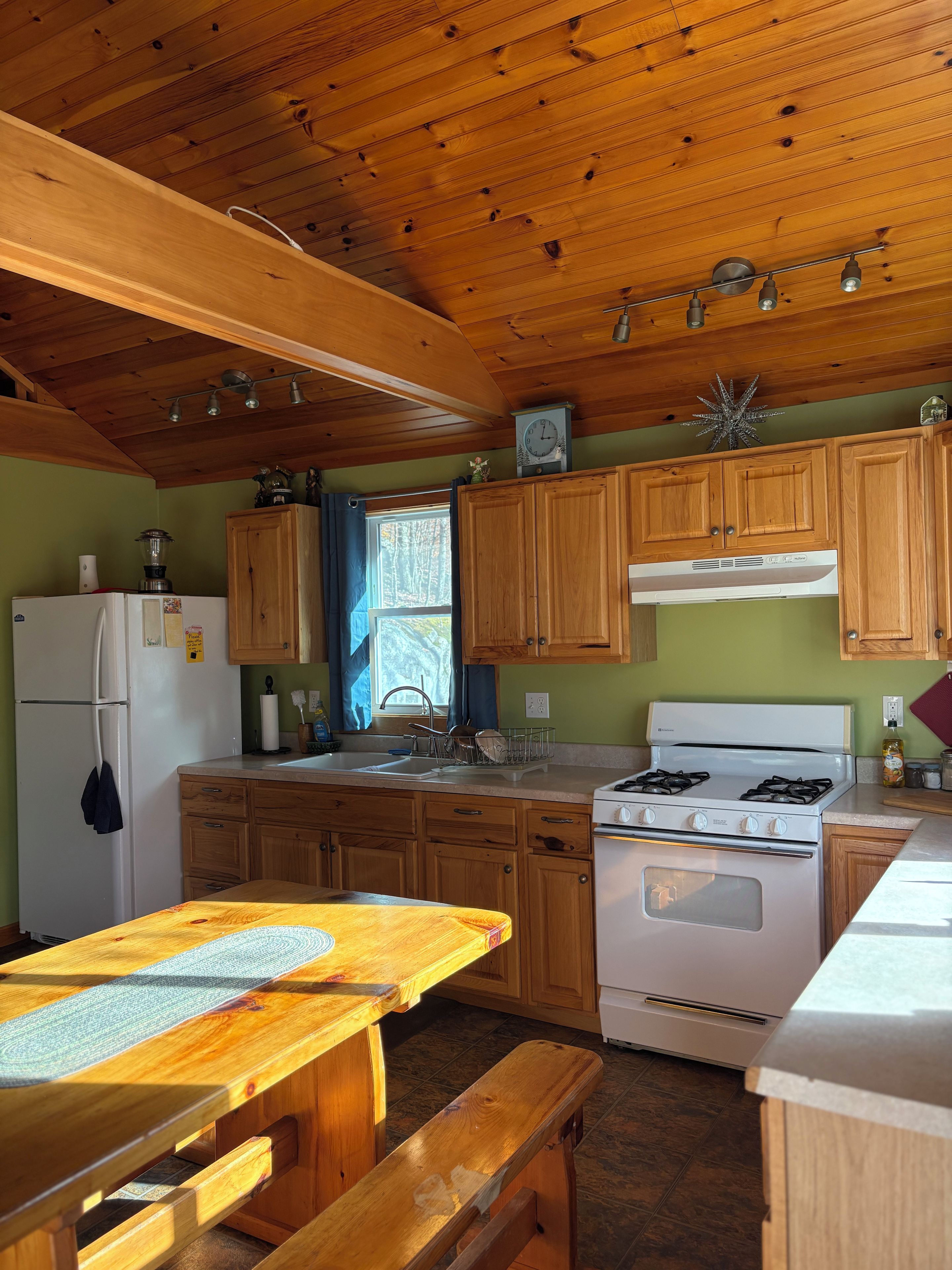A kitchen with wooden cabinets, a stove, a refrigerator, and a window with curtains.