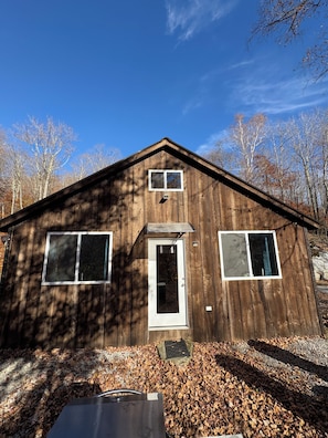 A wooden cabin with a front door, two windows, and a small porch area.