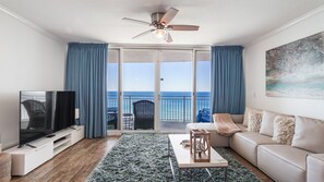 Un salon équipé d’un téléviseur, d’un canapé, d’une table basse et d’un balcon offrant une vue sur la mer.