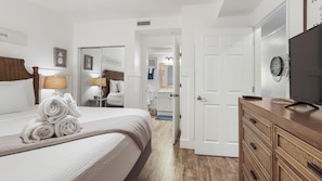 Une chambre d’hôtel avec un lit, une télévision, une commode en bois et une salle de bain visible à travers une porte ouverte.