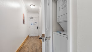 Una sala de bugaderia amb una rentadora i una assecadora, un terra de fusta i una porta blanca amb un cartell.