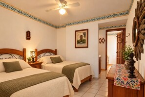 A room with two beds, a ceiling fan, a painting, a wooden cabinet, and a decorative wall piece.