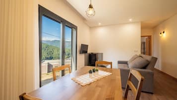 Una sala de estar moderna con una mesa de comedor de madera, un sofá gris y un televisor montado en la pared.
