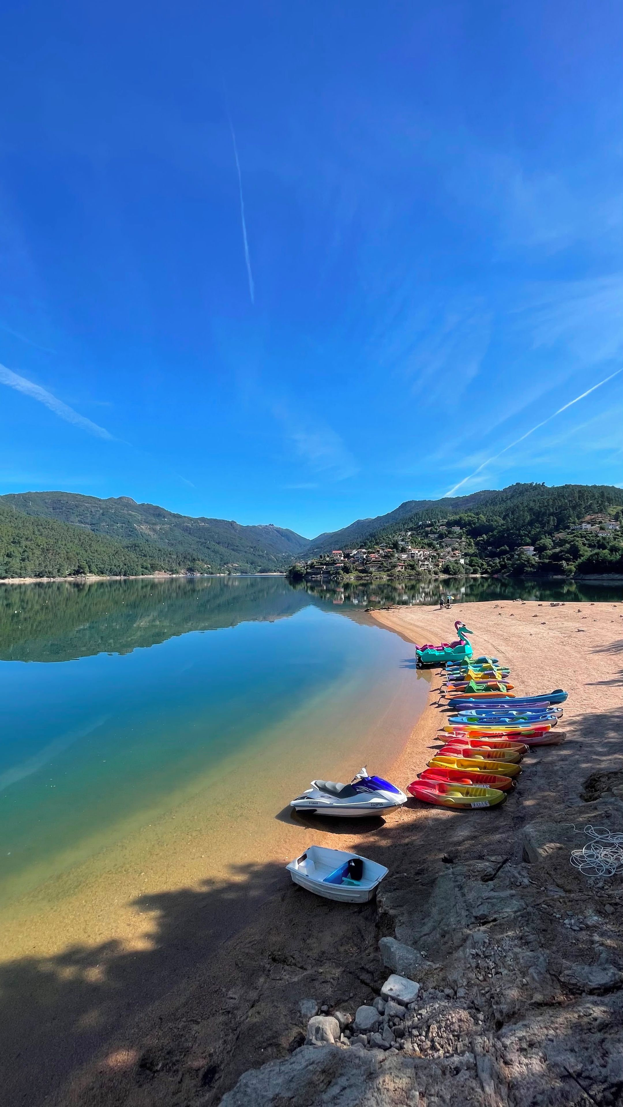 Un lago tranquilo con una hilera de kayaks coloridos y un bote en la orilla.