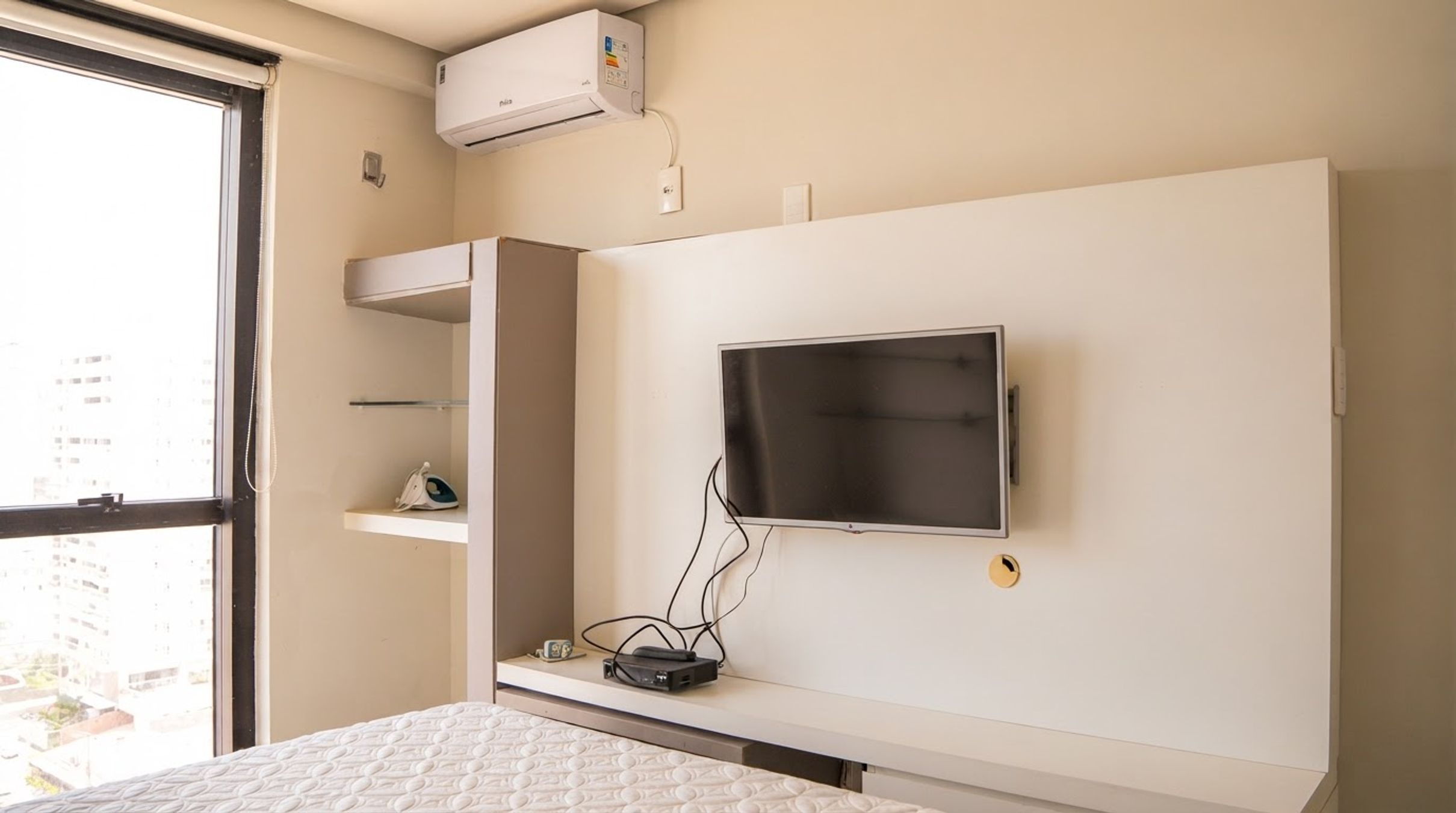 Un dormitorio con cama, televisor montado en la pared y equipo de aire acondicionado sobre la cama.