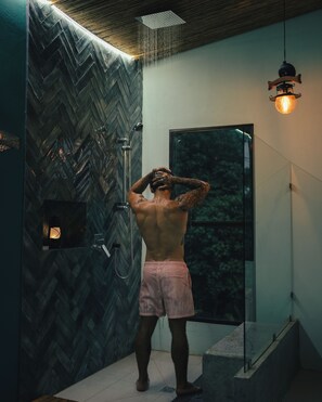 A person in a shower with a herringbone-patterned wall and a hanging light fixture. - Sukia Kin Glamping and Retreats (Drake Bay)