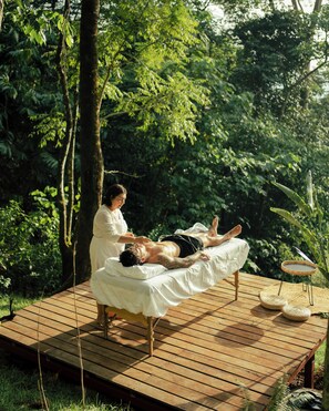 Une terrasse en bois avec une table de massage, une personne allongée dessus et une autre personne debout à côté.