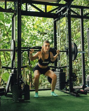 A person performing a squat exercise on a gym machine with a natural backdrop. - Sukia Kin Glamping and Retreats (Drake Bay)