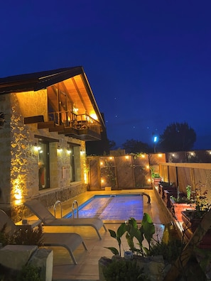 Ein zweistöckiges Gebäude mit Swimmingpool, Sitzgelegenheiten im Freien und Steinmauern.